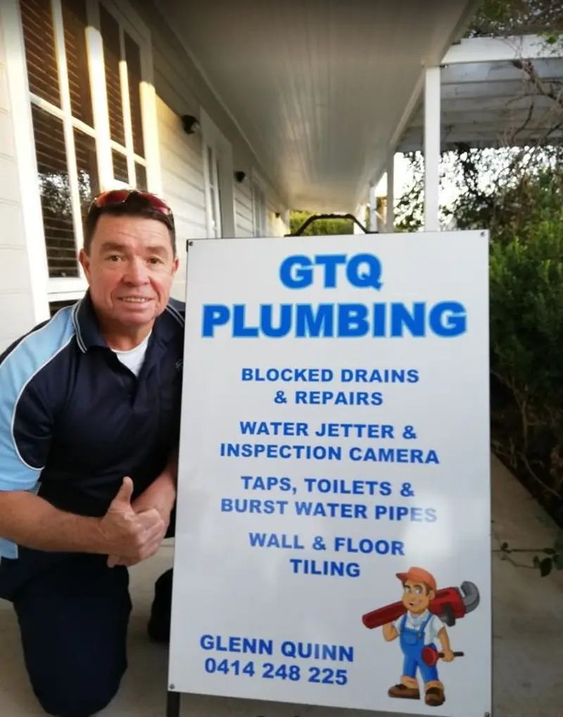 Glenn Quinn, licensed owner-operator of GTQ Plumbing, beside the Maitland Plumbing signboard listing blocked drains, water jetter, inspection camera, taps, toilets and burst water pipes.